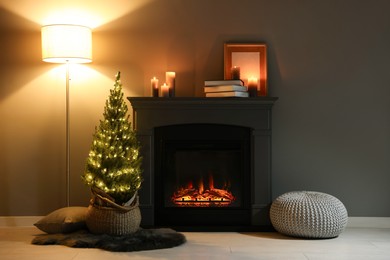 Photo of Small spruce tree in basket decorated with Christmas lights near fireplace indoors