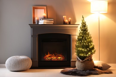 Photo of Small spruce tree in basket decorated with Christmas lights near fireplace indoors