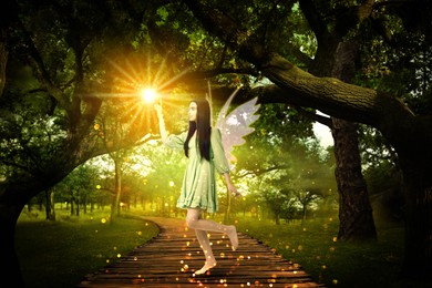 Image of Enchanting fairy touching magic light among trees. Mesmerizing girl with ethereal wings in charmed forest