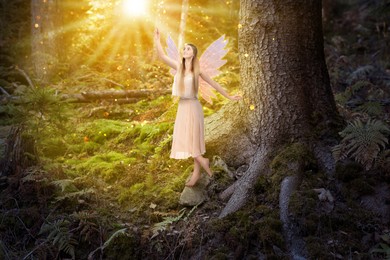 Image of Enchanting fairy touching magic light in forest. Mesmerizing girl with ethereal wings near tree