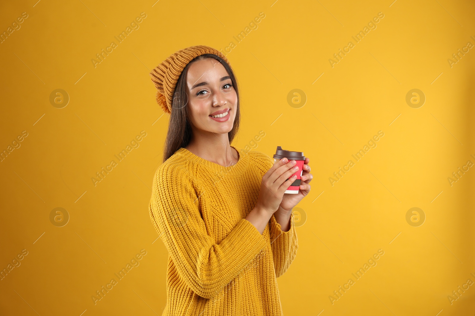 Photo of Happy beautiful woman with paper cup of mulled wine on yellow background