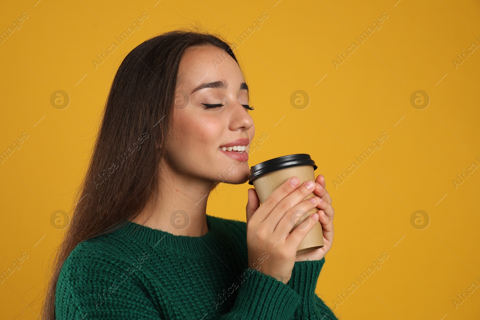 Photo of Happy beautiful woman with paper cup of mulled wine on yellow background