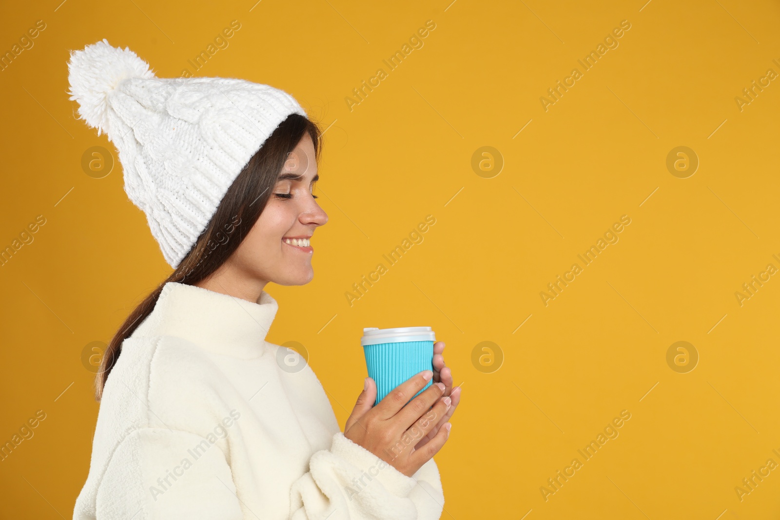 Photo of Happy beautiful woman with paper cup of mulled wine on yellow background. Space for text