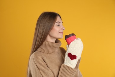 Photo of Happy beautiful woman with paper cup of mulled wine on yellow background