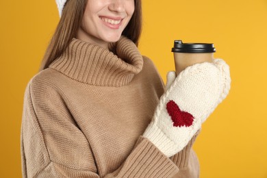 Photo of Happy beautiful woman with paper cup of mulled wine on yellow background, closeup