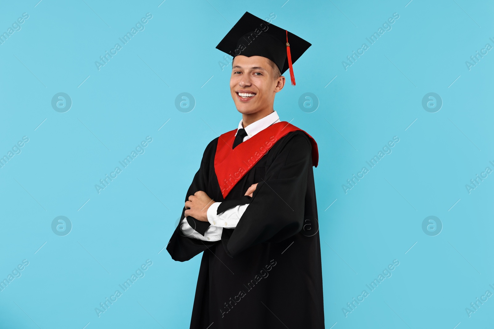 Photo of Happy student with crossed arms after graduation on light blue background