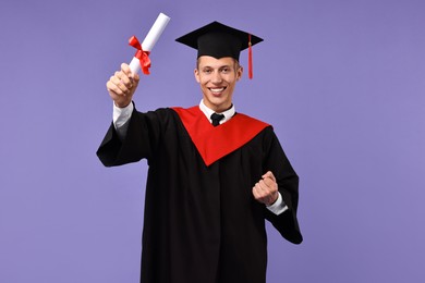 Photo of Happy student with diploma after graduation on violet background