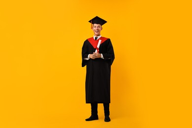 Photo of Happy student with diploma after graduation on orange background