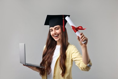 Photo of Happy student with laptop and diploma after graduation on grey background