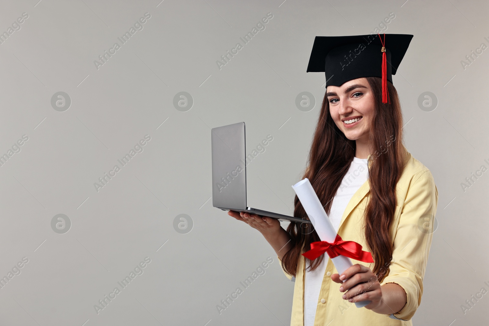 Photo of Happy student with laptop and diploma after graduation on grey background. Space for text