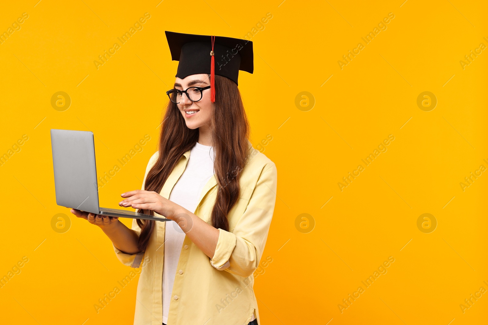 Photo of Happy student with laptop after graduation on orange background. Space for text