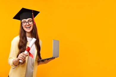 Photo of Happy student with laptop and diploma after graduation on orange background. Space for text