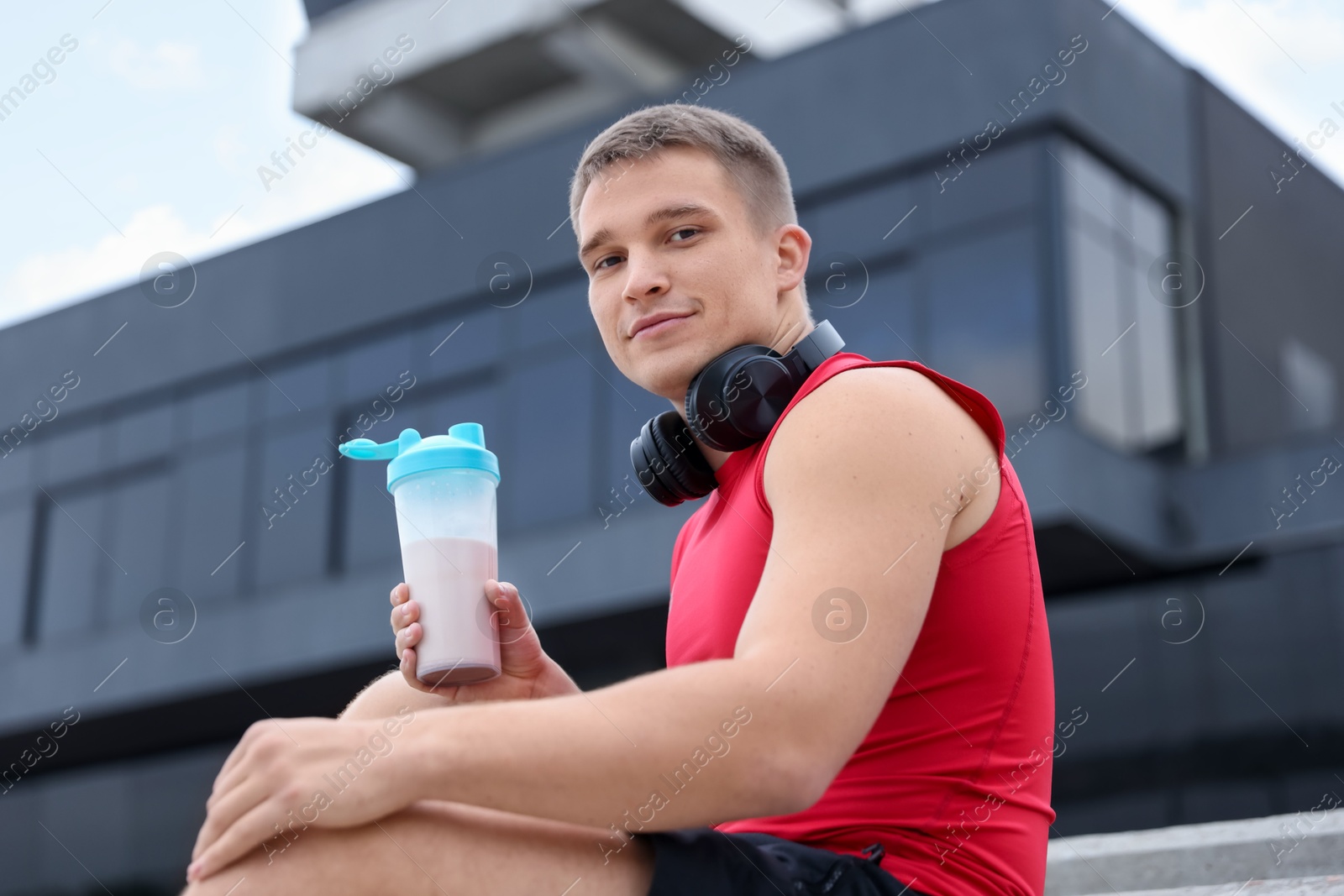 Photo of Athletic man with shaker of protein drink outdoors, low angle view