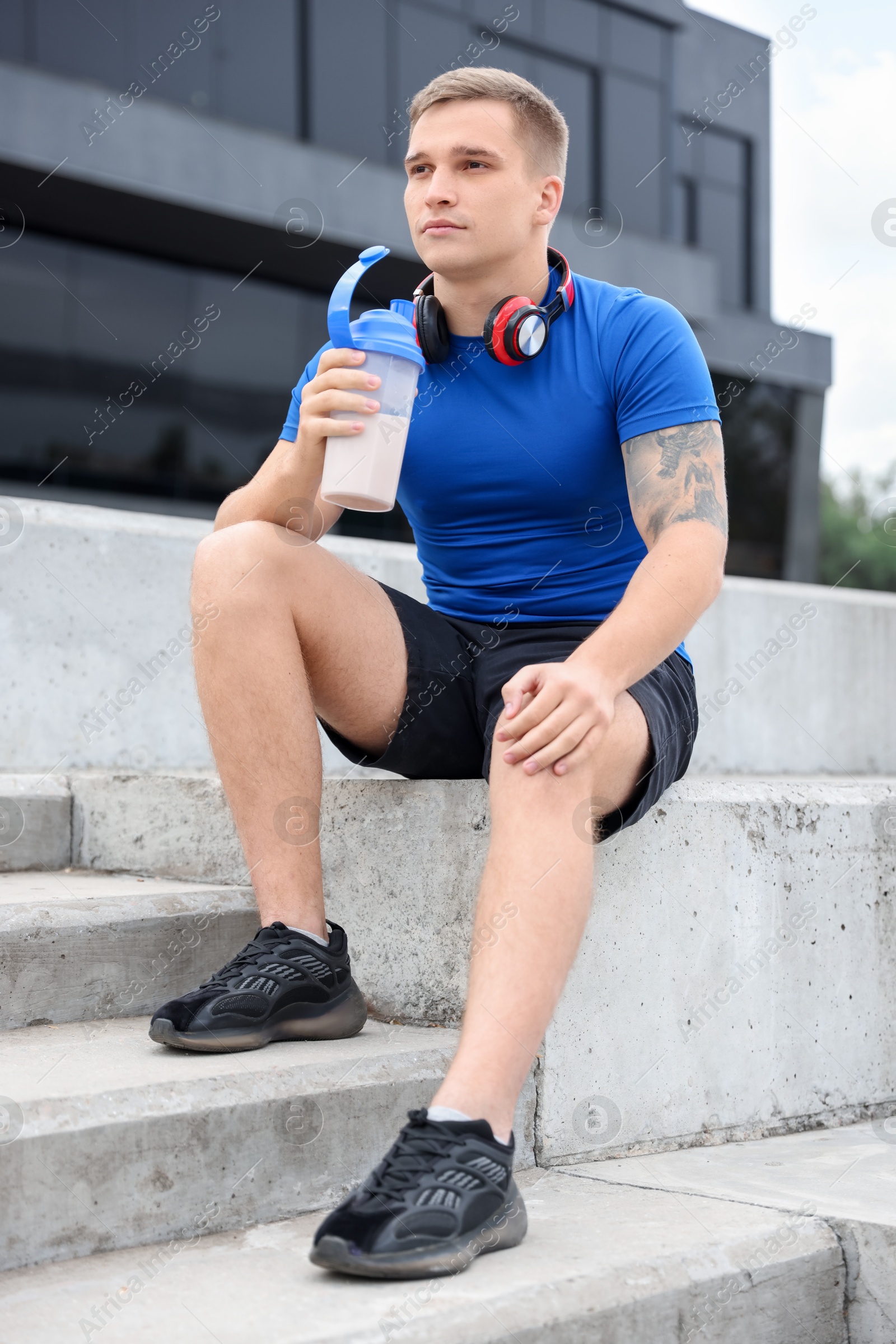 Photo of Athletic man with shaker of protein drink sitting on stairs outdoors