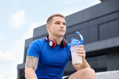 Photo of Athletic man with shaker of protein drink outdoors, low angle view