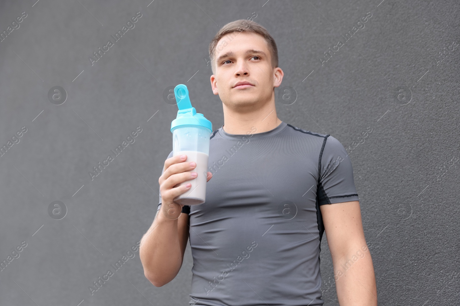 Photo of Athletic man with shaker of protein drink near grey wall