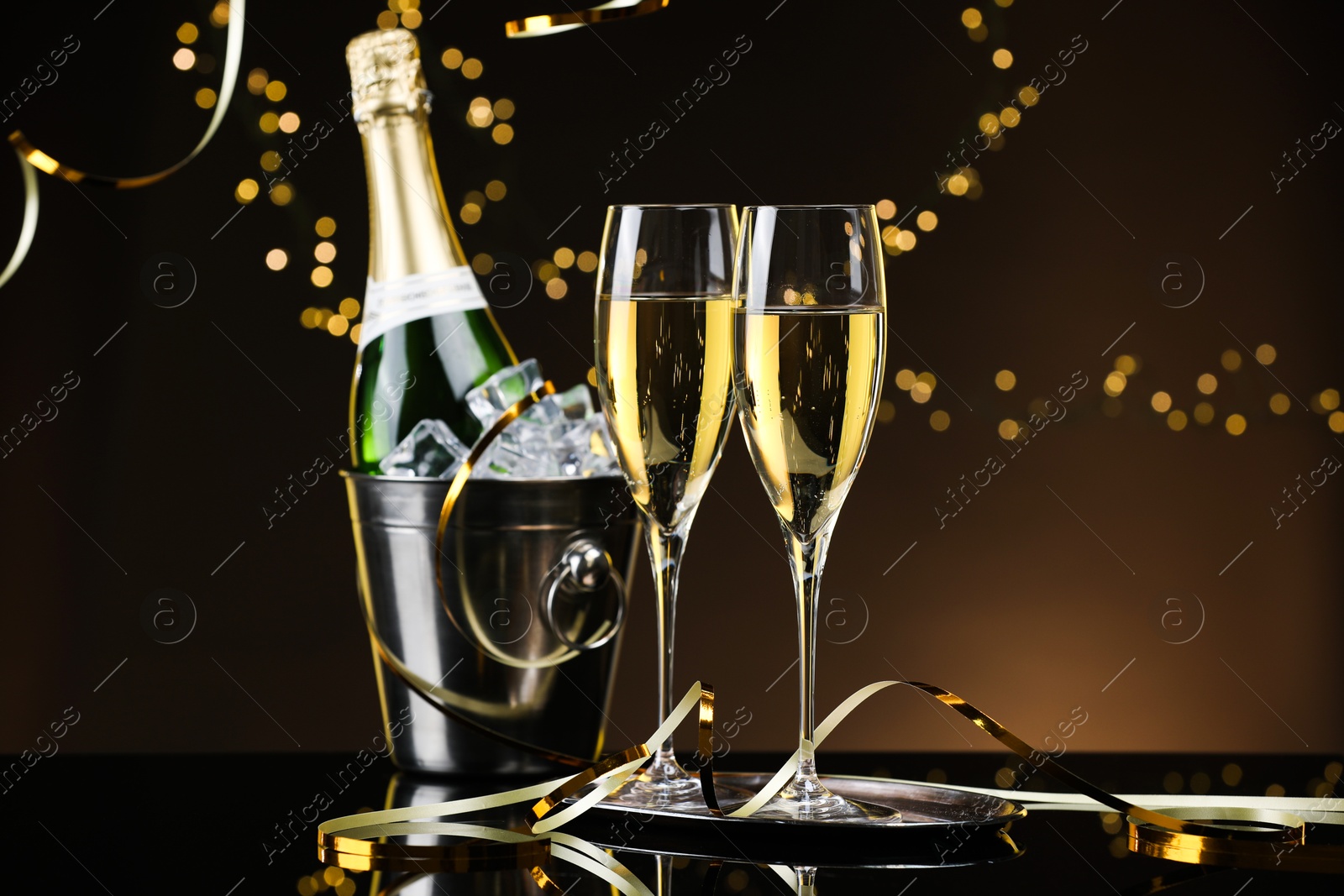 Photo of Champagne in glasses, bottle and cork on mirror surface against black background with blurred lights