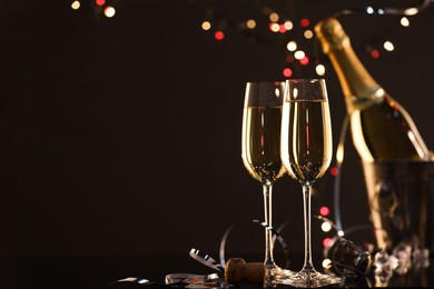 Photo of Champagne in glasses and ice bucket with bottle on black mirror surface, space for text