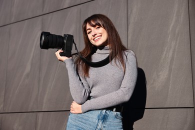 Professional photographer with digital camera near grey wall outdoors