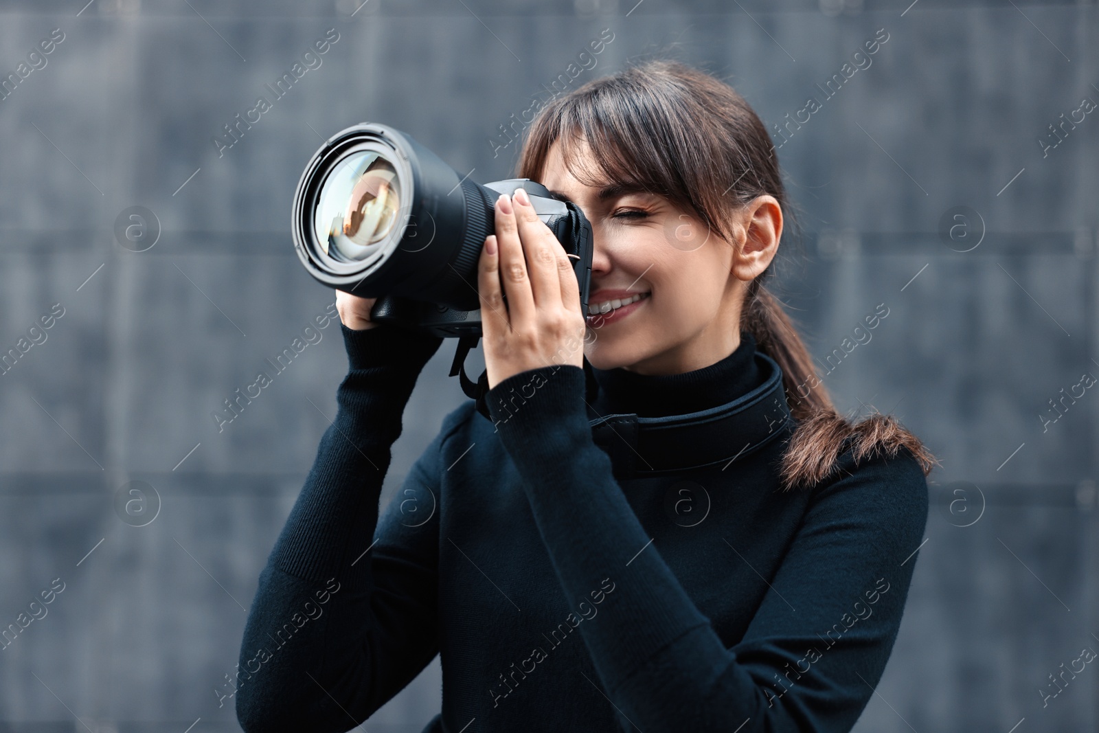 Photo of Professional photographer taking picture with camera near grey wall outdoors