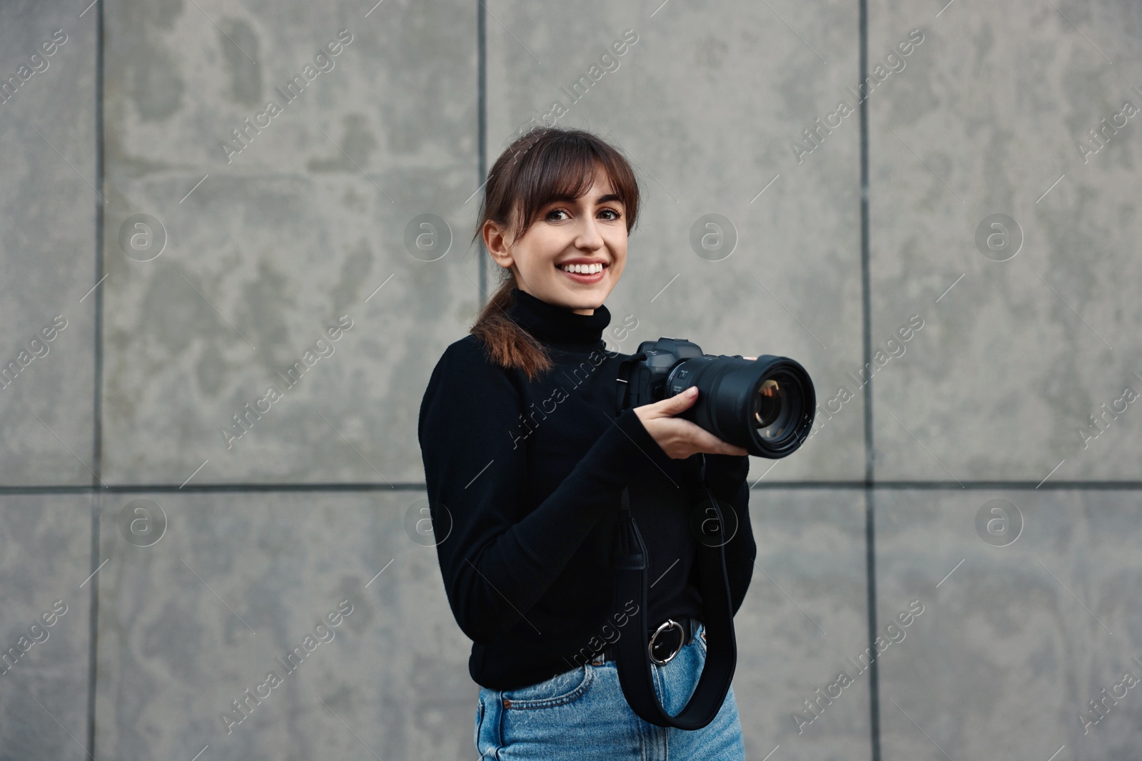 Photo of Professional photographer with digital camera near grey wall outdoors