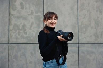 Photo of Professional photographer with digital camera near grey wall outdoors