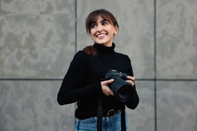 Photo of Professional photographer with digital camera near grey wall outdoors