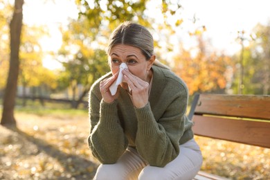 Photo of Woman with runny nose on wooden bench in park