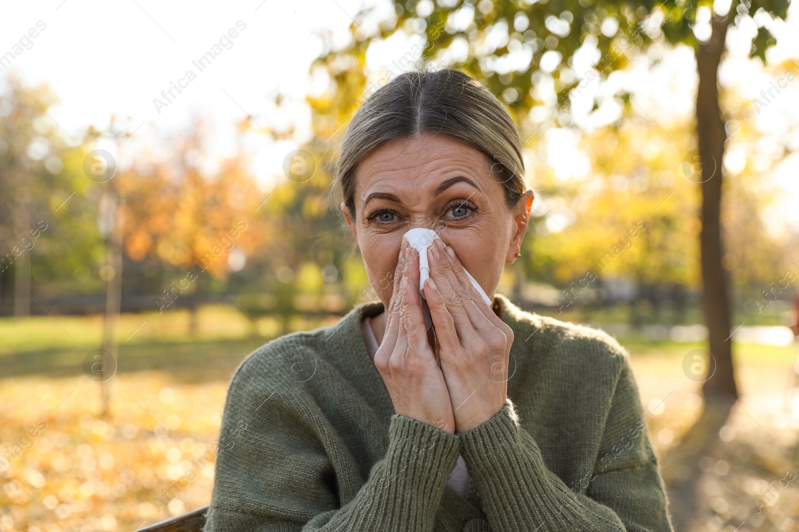 Photo of Woman with tissue blowing runny nose in park