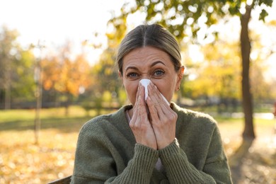 Photo of Woman with tissue blowing runny nose in park