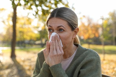 Photo of Woman with tissue blowing runny nose in park