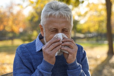 Photo of Senior man with tissue blowing runny nose in park