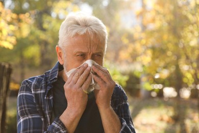 Senior man with runny nose in park, space for text