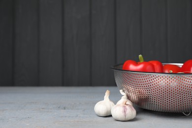 Photo of Stainless steel colander with vegetables and garlic on grey table, space for text. Cooking utensil