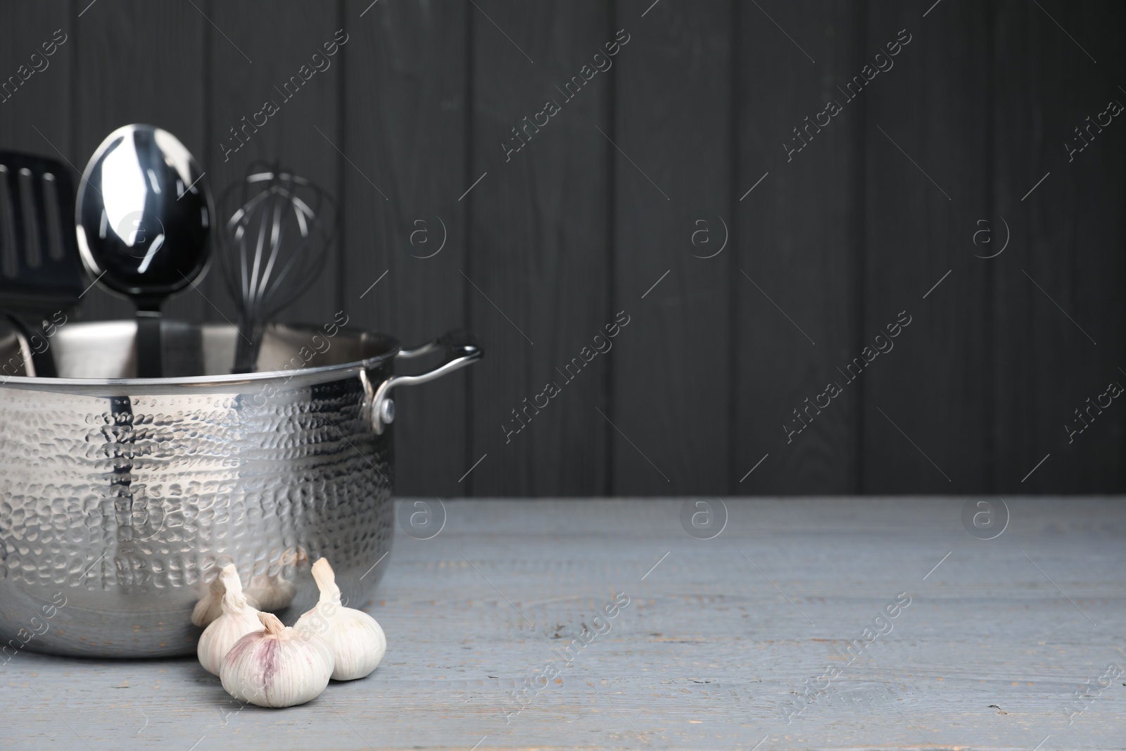 Photo of Dishware, cooking utensils and garlic on grey wooden table. Space for text