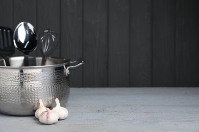 Dishware, cooking utensils and garlic on grey wooden table. Space for text