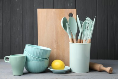 Dishware, cooking utensils and lemon on grey wooden table