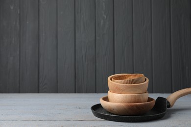 Bowls and frying pan on grey wooden table, space for text. Cooking utensils