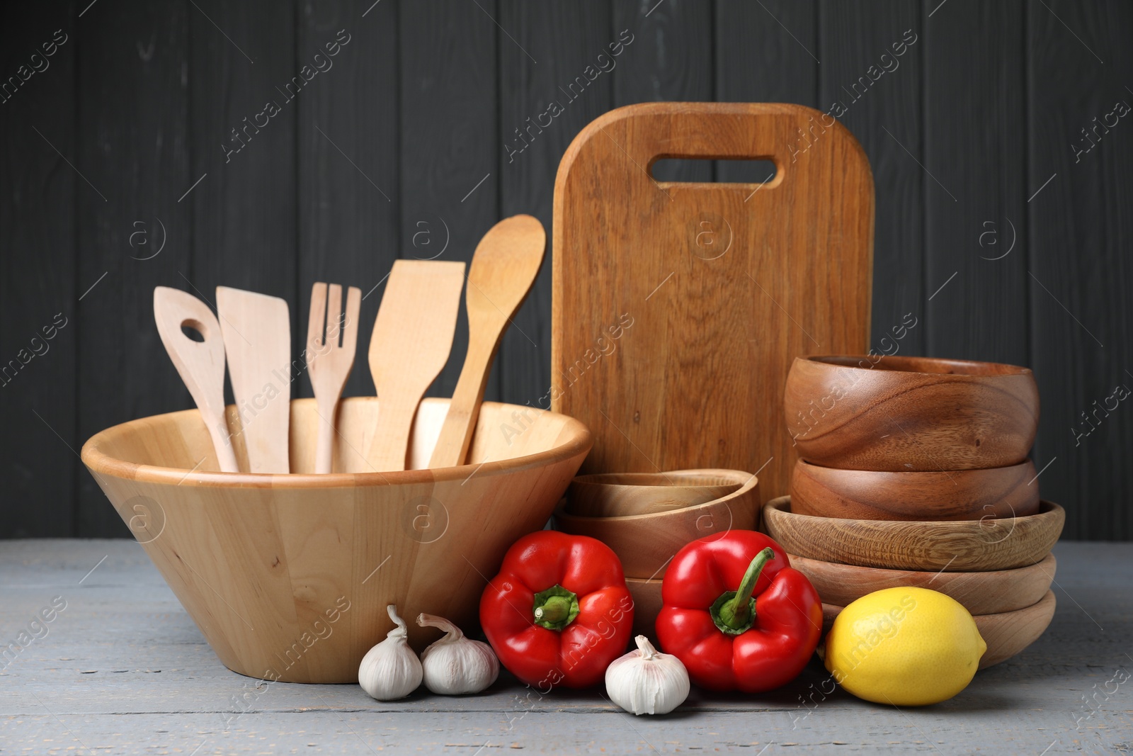 Photo of Dishware, cooking utensils, lemon, garlic and peppers on grey wooden table