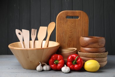 Dishware, cooking utensils, lemon, garlic and peppers on grey wooden table