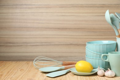 Photo of Dishware, cooking utensils, lemon and garlic on wooden table. Space for text