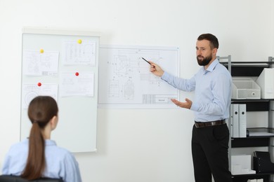 Photo of Man making presentation with engineering drawings to his colleagues in office