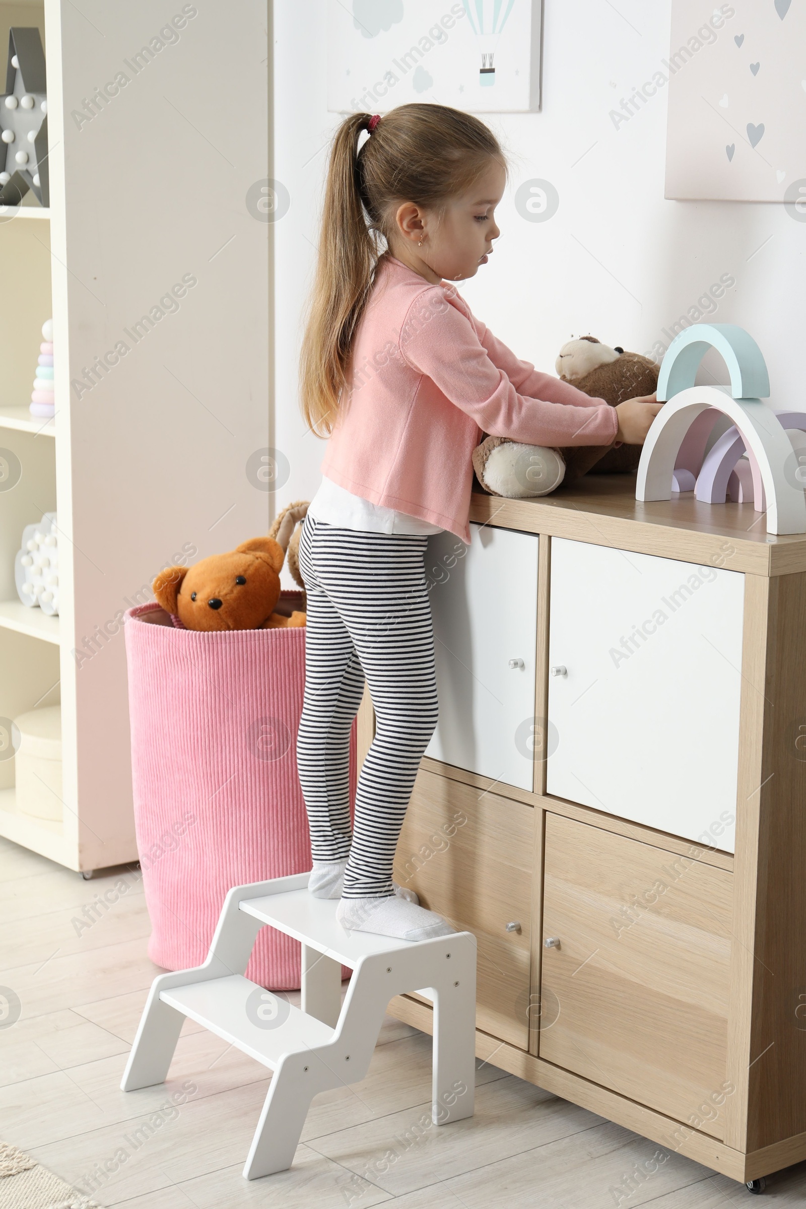 Photo of Little girl standing on step stool and playing with toys indoors