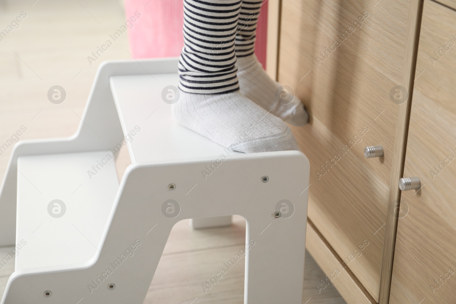 Photo of Little girl standing on step stool indoors, closeup