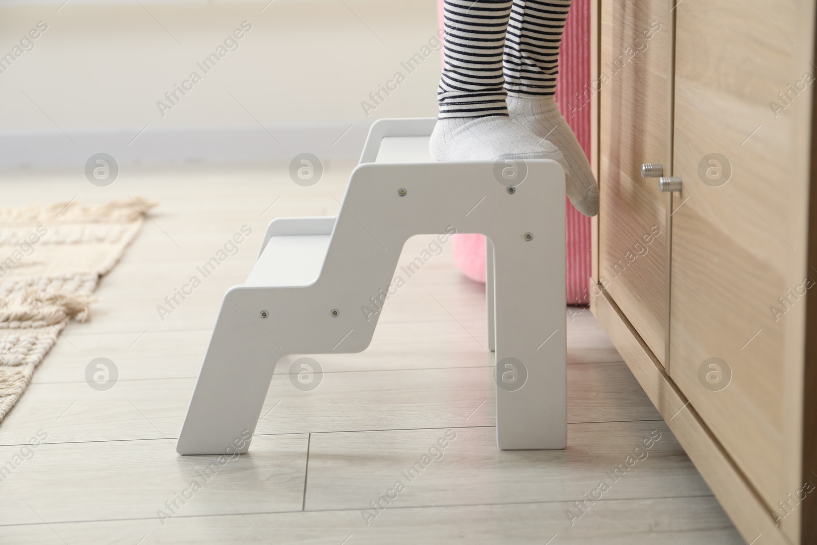 Photo of Little girl standing on step stool indoors, closeup