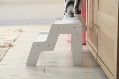 Photo of Little girl standing on step stool indoors, closeup