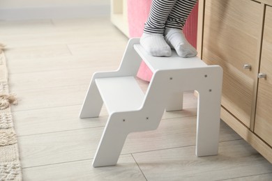 Photo of Little girl standing on step stool indoors, closeup