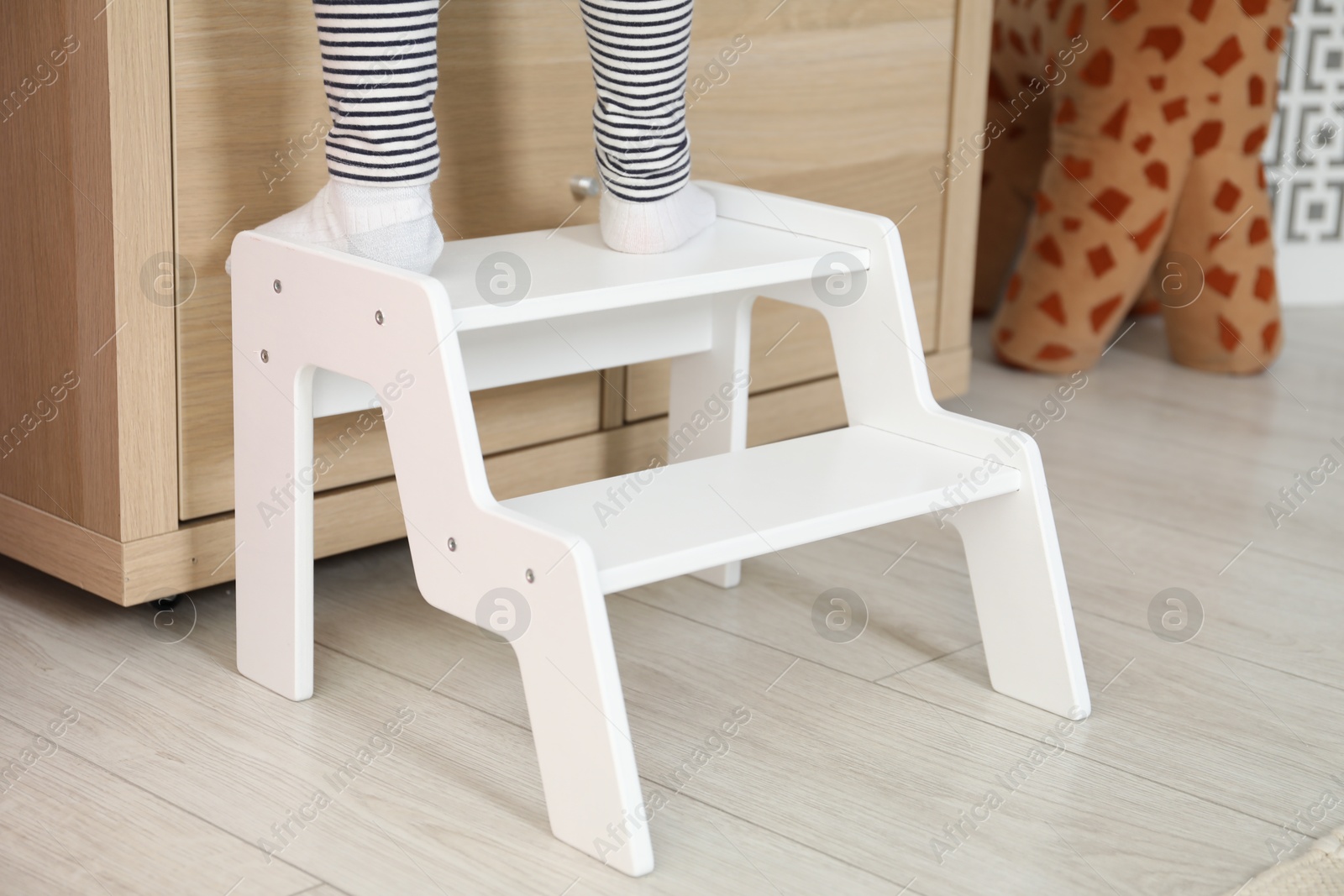 Photo of Little girl standing on step stool indoors, closeup