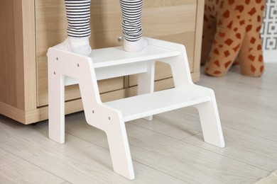 Photo of Little girl standing on step stool indoors, closeup