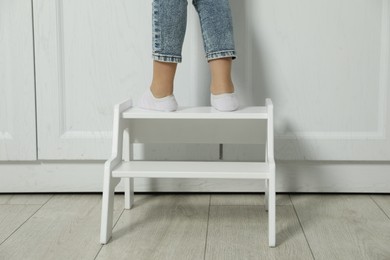 Photo of Little girl standing on step stool indoors, closeup